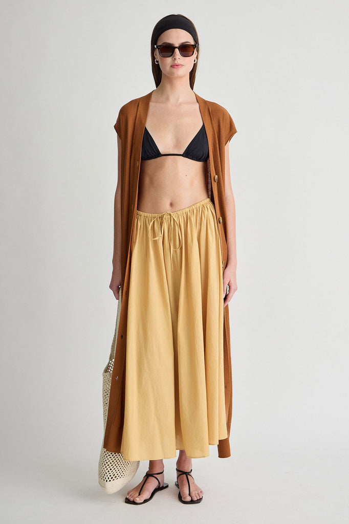 Woman wearing a mustard yellow skirt, black bikini top, and brown cardigan on a white background