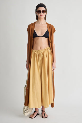Woman wearing a mustard yellow skirt, black bikini top, and brown cardigan on a white background