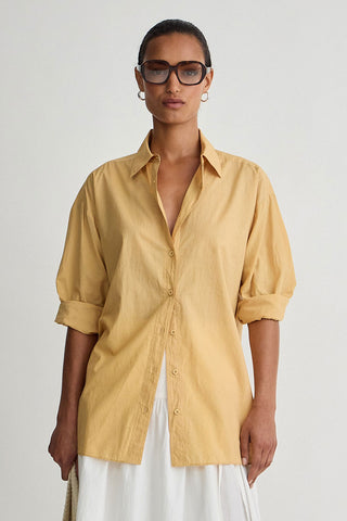 Woman wearing a mustard yellow shirt and white pants on a plain background