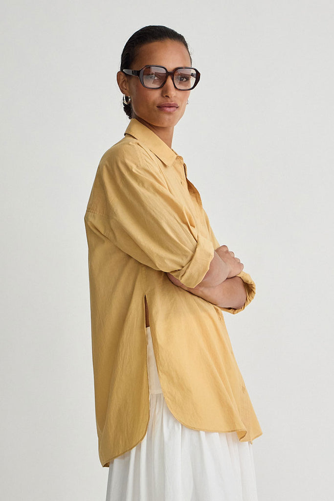 Person wearing a yellow shirt and white pants on a plain background