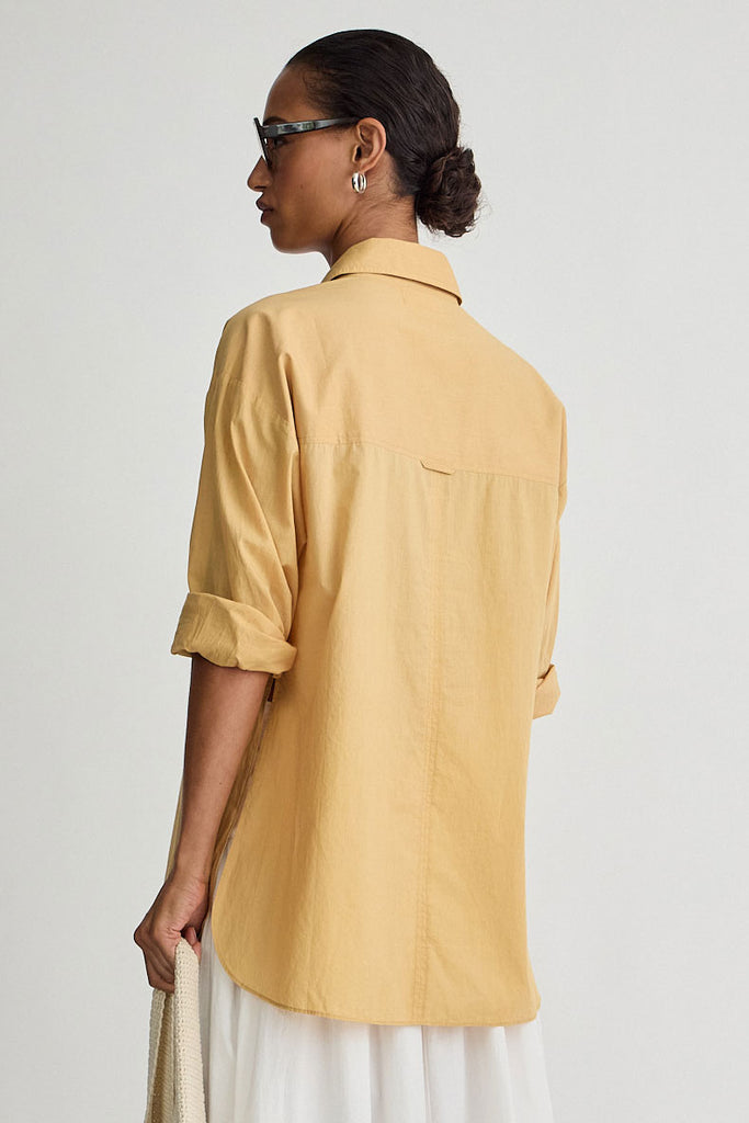Woman wearing a mustard yellow shirt on a plain background