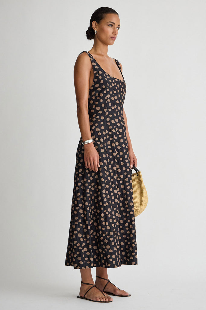 Woman wearing a black floral dress holding a straw bag on a white background