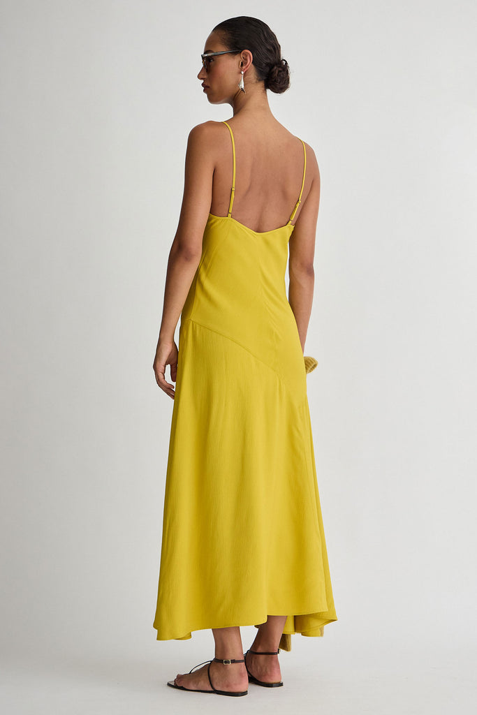 Woman wearing a yellow dress with thin straps on a plain background