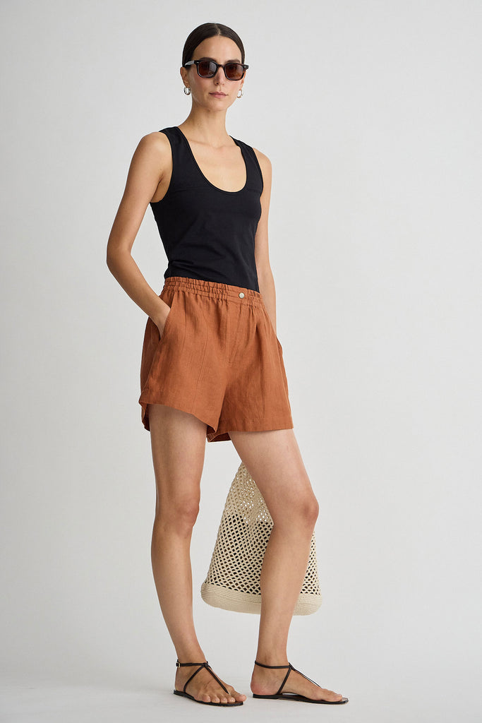 Woman wearing a black tank top and brown shorts on a plain background