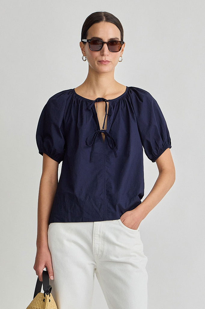 Woman wearing a navy blue blouse with puff sleeves against a plain background