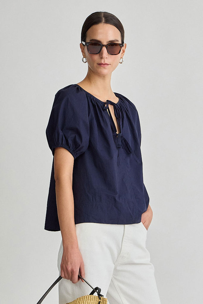 Woman wearing a navy blue blouse and white pants against a plain background