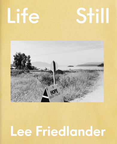 Book cover of 'Life Still' by Lee Friedlander with a black and white photo of a road sign in a field.