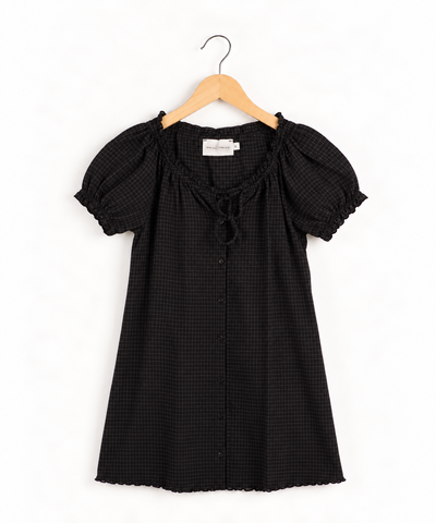 Black and white micro-check mini dress with short puff sleeves, a ruffled scoop neckline featuring a front tie detail, and a button-down front hanging on a wooden hanger against a white background.