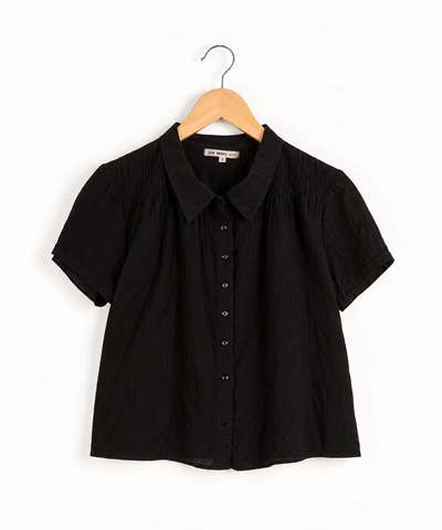 black ruffled blouse on a wooden hanger against white wall