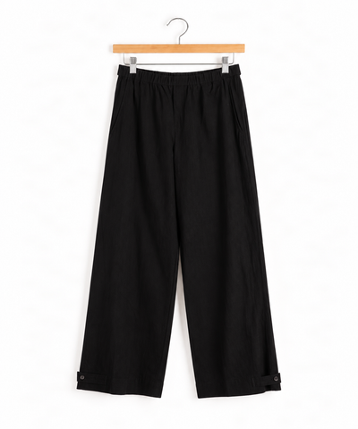 black wide leg pant with snap closure on the ankles hanging from wooden hanger on white wall