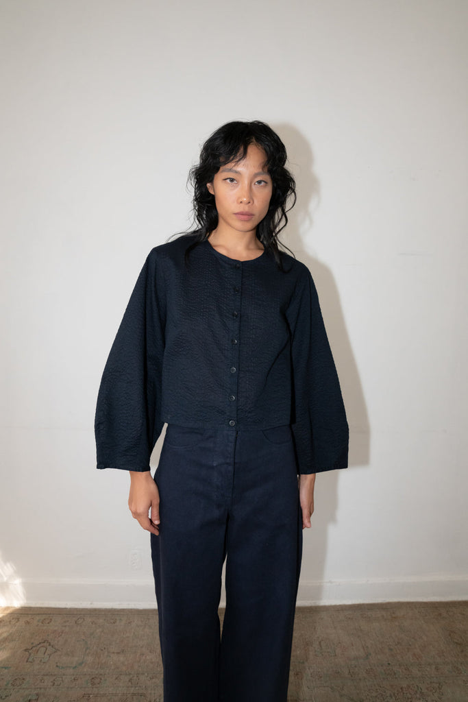  Woman wearing a textured dark navy cropped long-sleeve button-up top with wide sleeves, paired with matching dark navy trousers.