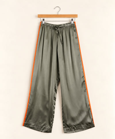 sage green silk pants with orange stripe on sides, hanging from hanger on cream background