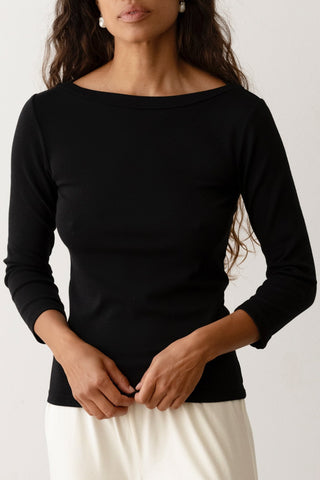 Person wearing a boatneck top in black with white pants against white background