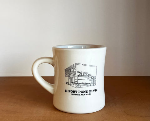 White mug with dark green graphic and text on a brown surface