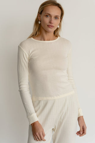 A person wearing an off-white, long-sleeved thermal top with a boat neckline and ribbed sleeves.