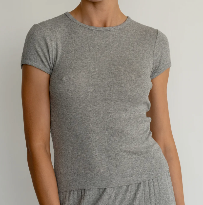 A woman wearing a short-sleeve crew-neck t-shirt in heather gray, shown from the neck down against a plain light background.