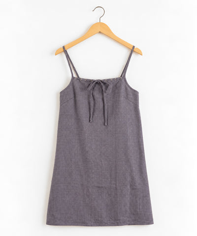 A grey and black check mini slip dress with double camisole straps and a front tie detail hanging on a wooden clothes hanger.