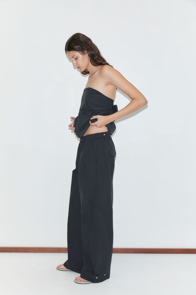 Woman wearing a black strapless top and wide-leg pants against a white background