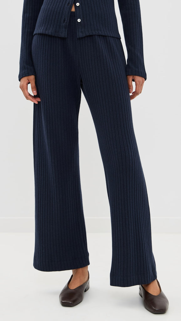 Mid-section view of a person wearing dark navy blue ribbed knit wide-leg pants paired with a matching buttoned cardigan and dark brown leather flat shoes.