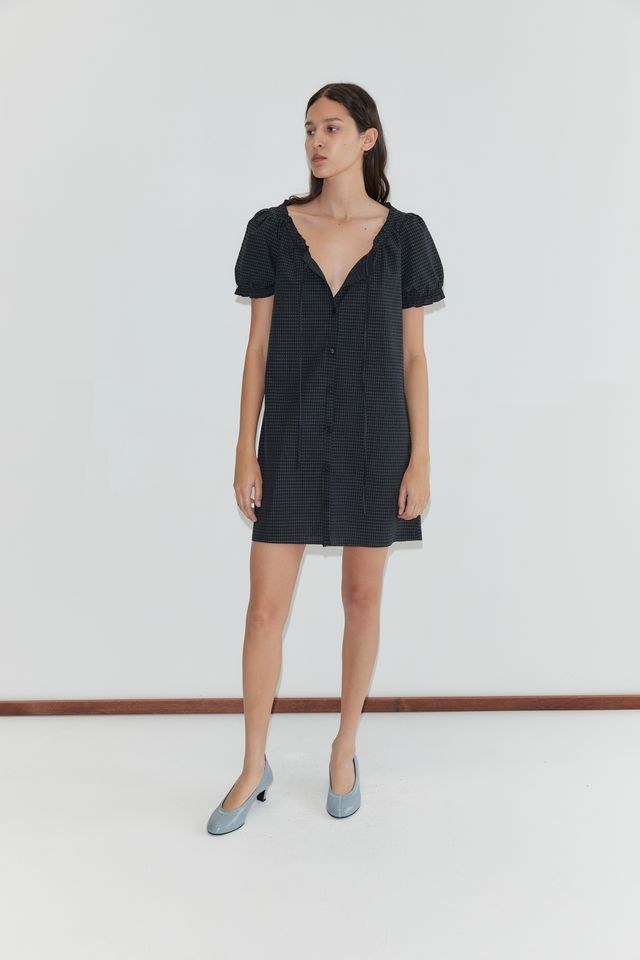Model wearing a black and white grid patterned mini dress with short puff sleeves, button front, and blue kitten heel pumps.