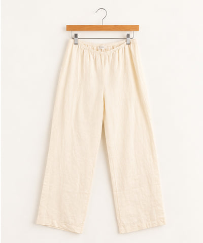 cream-colored cotton pajama pants with an elastic waistband, hanging from a wooden hanger shown flat against a solid white background.