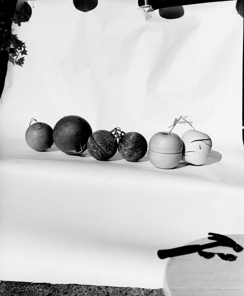 Row of vintage fishing buoys and net floats in various sizes on a white studio background, black and white photography.